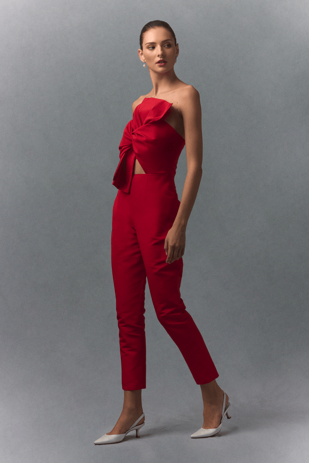 Woman wearing a red strapless jumpsuit with a bow detail on a gray background