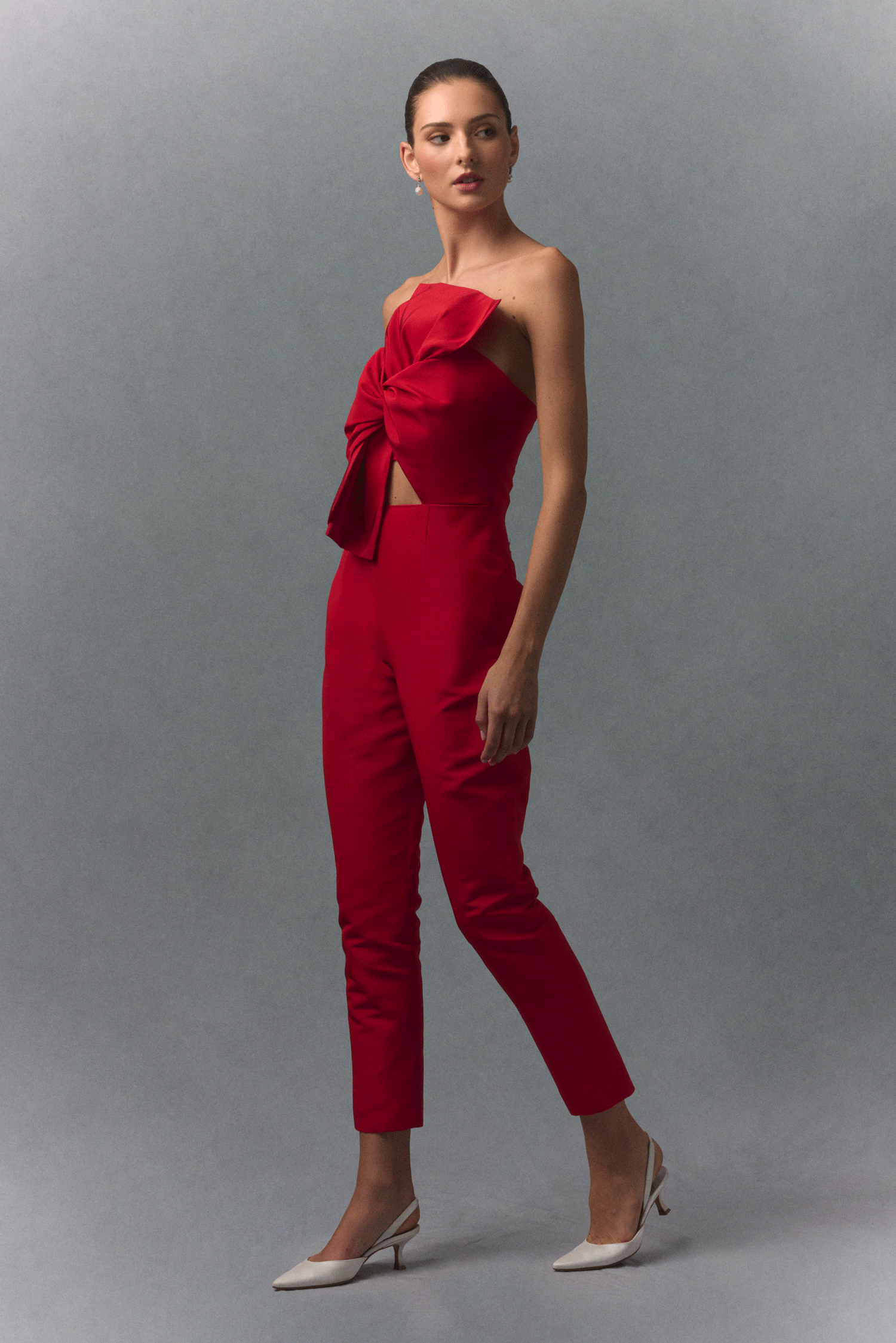 Woman wearing a red strapless jumpsuit with a bow detail on a gray background