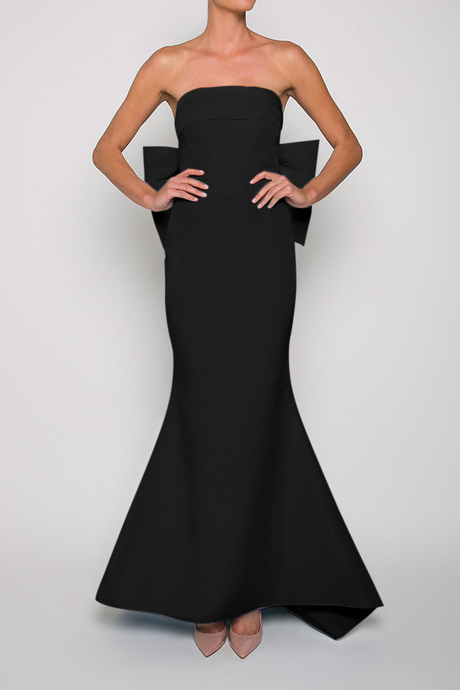 A model wearing a black strapless, floor-length silk faille mermaid gown with a straight neckline, fitted bodice with boning, an oversized bow back, and a slight back train.